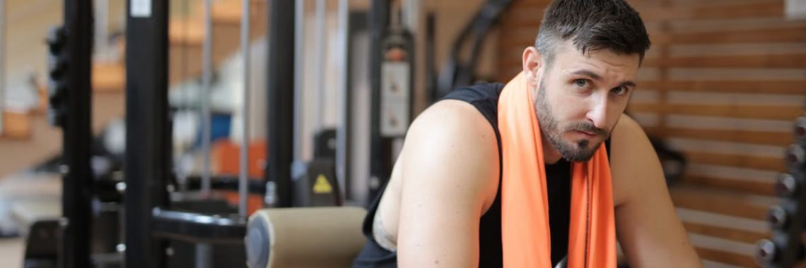 Adult male resting in a gym with an orange towel after strength training.